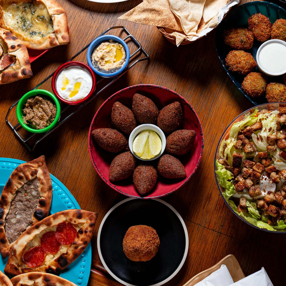 Mesa com esfihas, homus, quibes, salada e acompanhamentos árabes