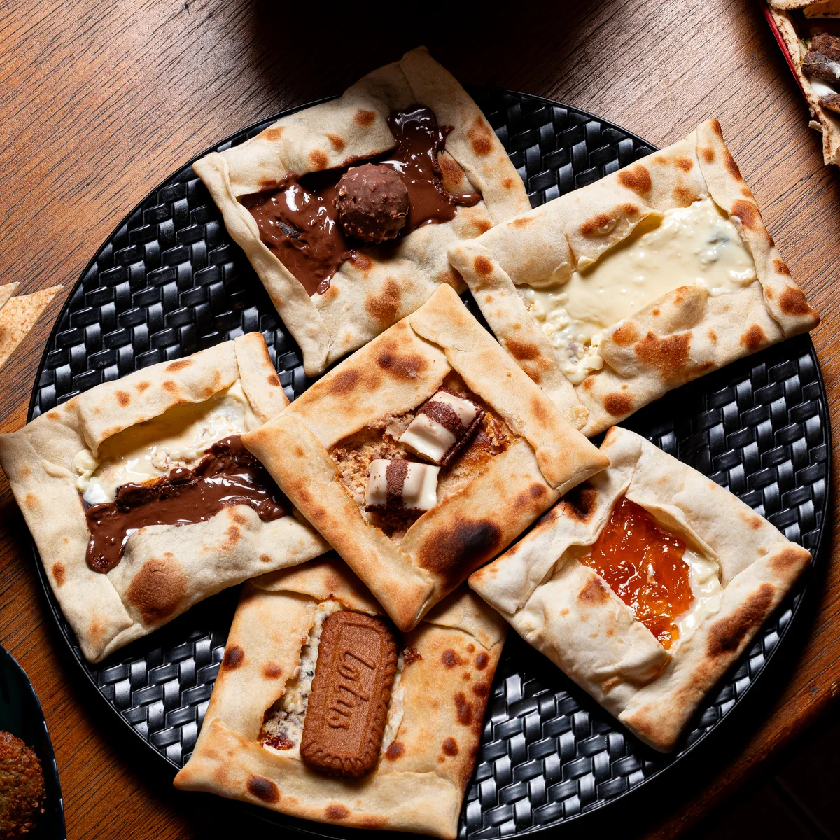 Esfihas doces e salgadas servidas em uma bandeja, com salada e shawarma ao fundo