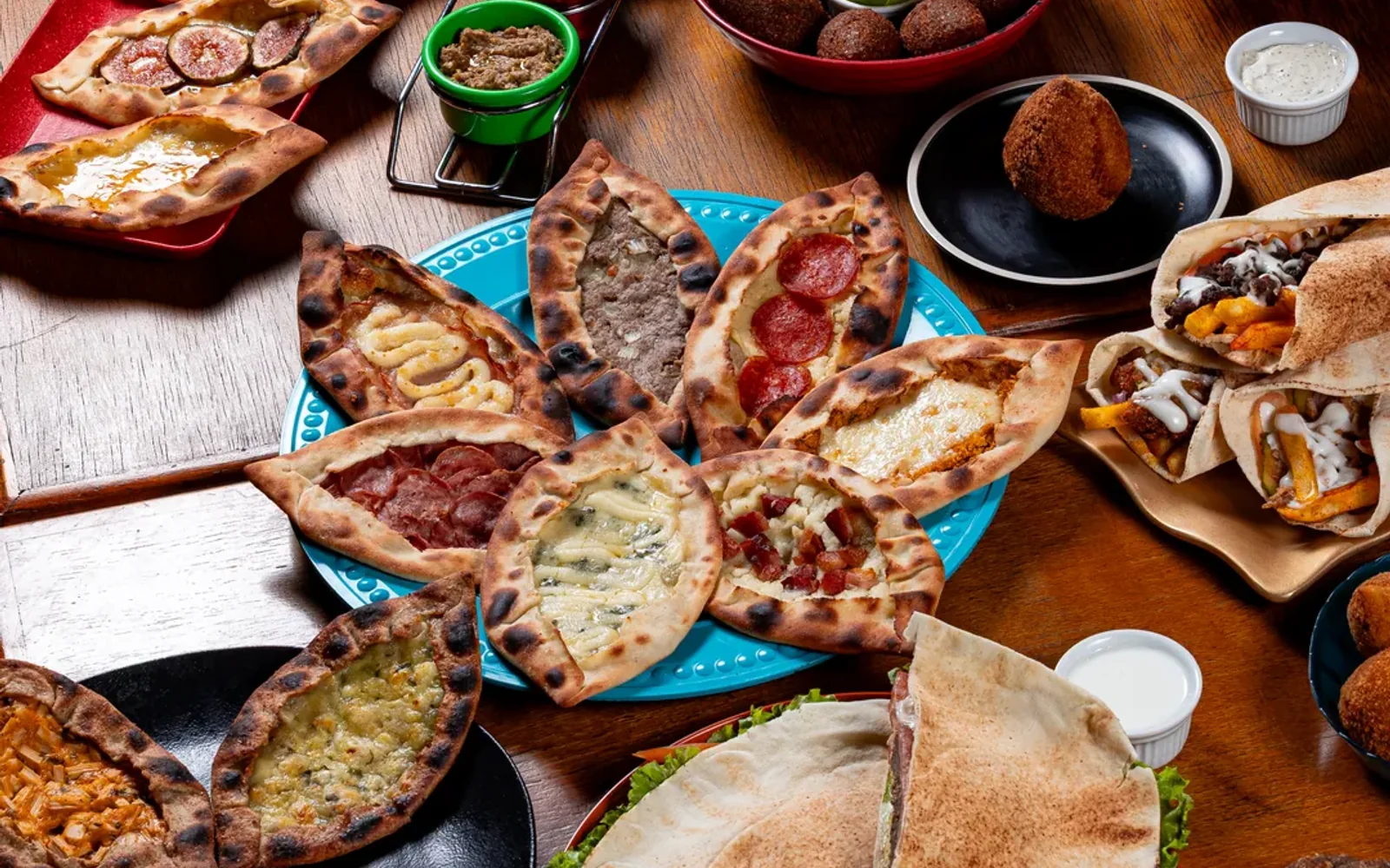 Mesa farta com esfihas, quibes, shawarmas e acompanhamentos árabes